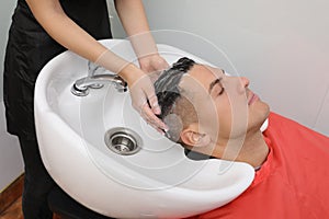 Professional hairdresser washing client`s hair at sink in salon, closeup