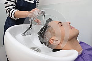 Professional hairdresser washing client`s hair at sink in salon, closeup