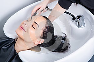 Professional hairdresser washing hair of young woman in beauty salon