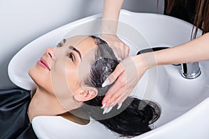 Professional hairdresser washing hair of young woman in beauty salon