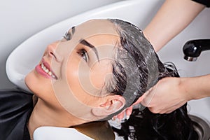 Professional hairdresser washing hair of young woman in beauty salon