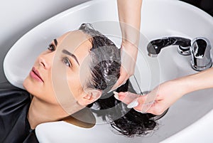 Professional hairdresser washing hair of young woman in beauty salon