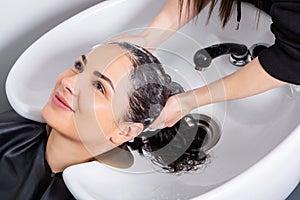 Professional hairdresser washing hair of young woman in beauty salon