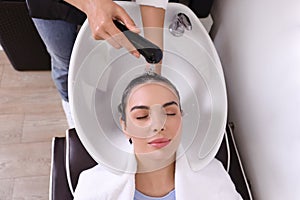 Professional hairdresser washing woman`s hair in beauty salon, above view