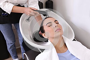 Professional hairdresser washing woman`s hair in beauty salon, closeup