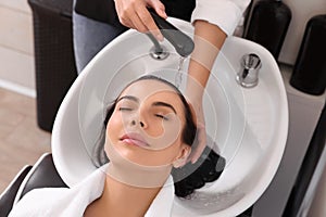 Professional hairdresser washing woman`s hair in beauty salon, closeup