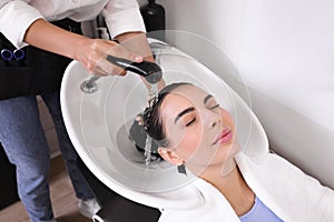 Professional hairdresser washing woman`s hair in beauty salon, closeup