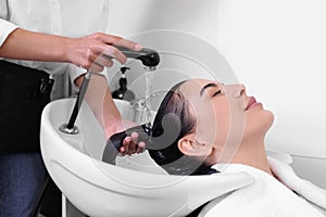 Professional hairdresser washing woman`s hair in beauty salon, closeup