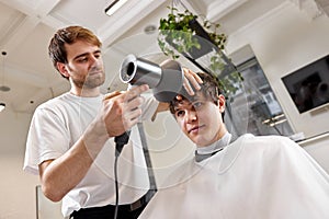 Professional hairdresser during work with man client with hair dryer