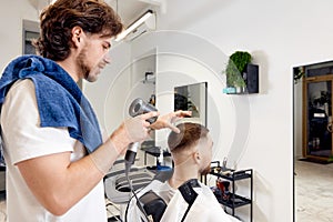 Professional hairdresser during work with man client with hair dryer