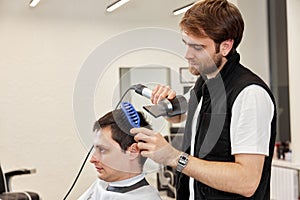 Professional hairdresser during work with man client with hair dryer