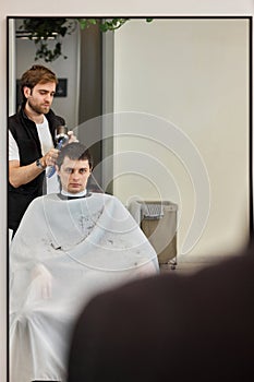 Professional hairdresser during work with man client with hair dryer