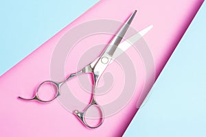 Professional hairdressing scissors close-up on blue and pink background top view.