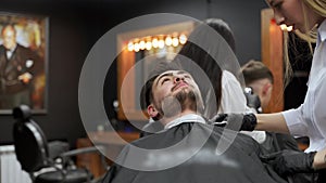 Professional hairstylist gives client precision beard trim in modern barbershop. Skillful barber uses scissors, comb