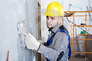 Professional in the helmet is plastering the wall