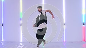 Professional hip hop dancer practicing street dance elements against bright neon lights in studio. Stylish man dancing