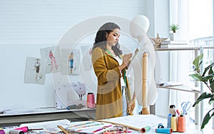 Professional hipster female tailor wearing modern yellow suit, measuring mannequin in shop, room, home studio, making, designing
