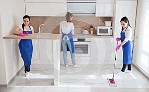 Professional house cleaning. Three beautiful girls are cleaning the kitchen. The girl washes the floor.