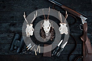 Professional hunters equipment for hunting. Rifle, knives, trophy sculps, ammunition, and others on a wooden black background. Tro