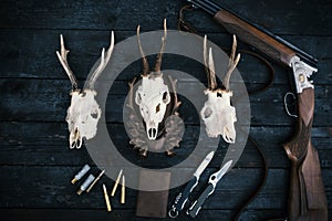 Professional hunters equipment for hunting. Rifle, knives, trophy sculps, ammunition, and others on a wooden black background. Tro