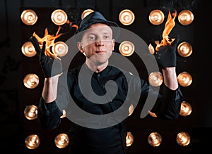 Professional illusionist in black hat, shirt and glowes playing with fire