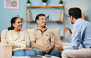 Professional Indian banker explaining about insurance policy to senior couple at home - concept of financial advisor