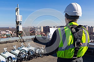 Professional industrial climber in helmet and uniform reads technical documentation and antennas of GSM DCS UMTS LTE