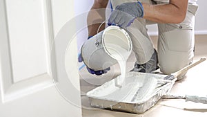 Professional interior construction worker pouring white color paint to tray