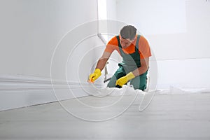 Professional janitor cleaning baseboard with brush after renovation