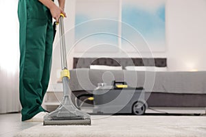 Professional janitor removing dirt from carpet with vacuum cleaner in bedroom, closeup