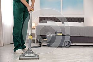 Professional janitor removing dirt from carpet with vacuum cleaner in bedroom. Space for text