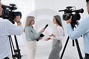 Professional journalist interviewing young business woman and cameramen shooting video for broadcast