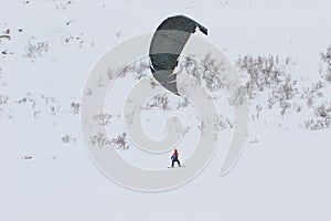 Professional kite boarding rider sportsman with kite in sky rides in snow on kiteboard. Recreational activity, extreme active