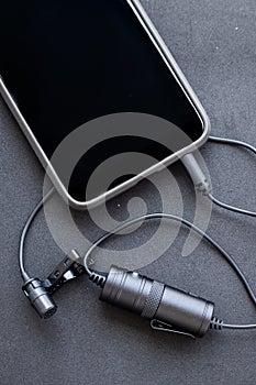 Professional lavalier or lapel microphone on a black surface. close-up, portrait view . The details of the grip clip or bra,