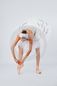 Professional legs of a young ballerina who puts on pointe shoes isolated on a white background in the studio. Ballet practice.