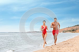 Professional lifeguards running at sandy beach on sunny day