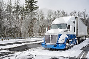 Professional long haul big rig semi truck with reefer semi trailer standing for rest on the winter truck stop parking lot with