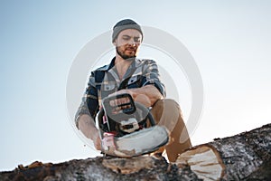 lumberman wearing plaid shirt sawing tree with chainsaw on sawmill