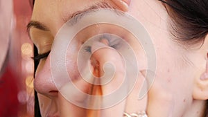 A professional make-up artist applies shiny bodily eyeshadow with a special brush in a make-up studio