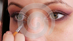 A professional make-up artist applies shiny bodily eyeshadow with a special brush in a make-up studio