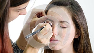 Professional make-up artist applying eyeshadow to model eye using special brush. Natural makeup in salon. Beauty, makeup