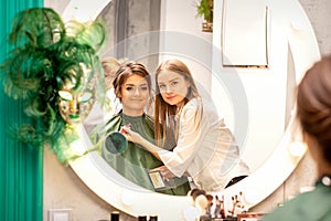 Professional make up artist and beautiful girl looking in the mirror smiling in a beauty salon.