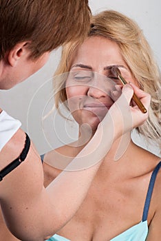 Professional make-up artist doing makeup to a blonde behind the scenes