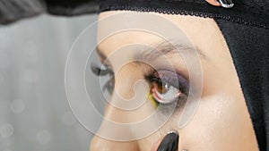 Professional make-up artist pastes false long black eyelashes on the model eye, which is colored with different color