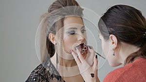 Professional makeup artist applies makeup to a beautiful model. Colors of red lipstick. Close-up