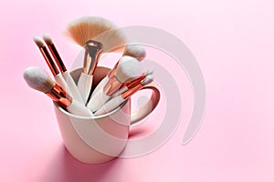 Professional makeup brushes in cup on pink background