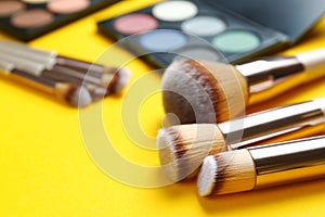 Professional makeup brushes and eye shadow palette on yellow background