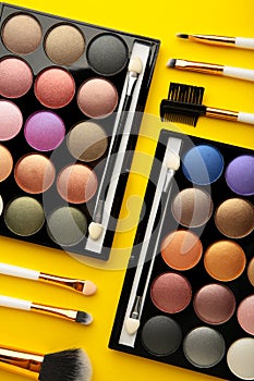 Professional makeup palette with brushes on yellow background. Vertical photo