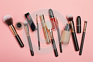 Professional makeup products with cosmetic beauty products, blushes, eye liner, eye lashes, brushes and tools on pink background