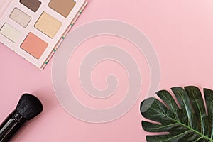 Professional makeup tools palette of multicolor cosmetic make up with a monstera leaf and a powder brush on pink background.